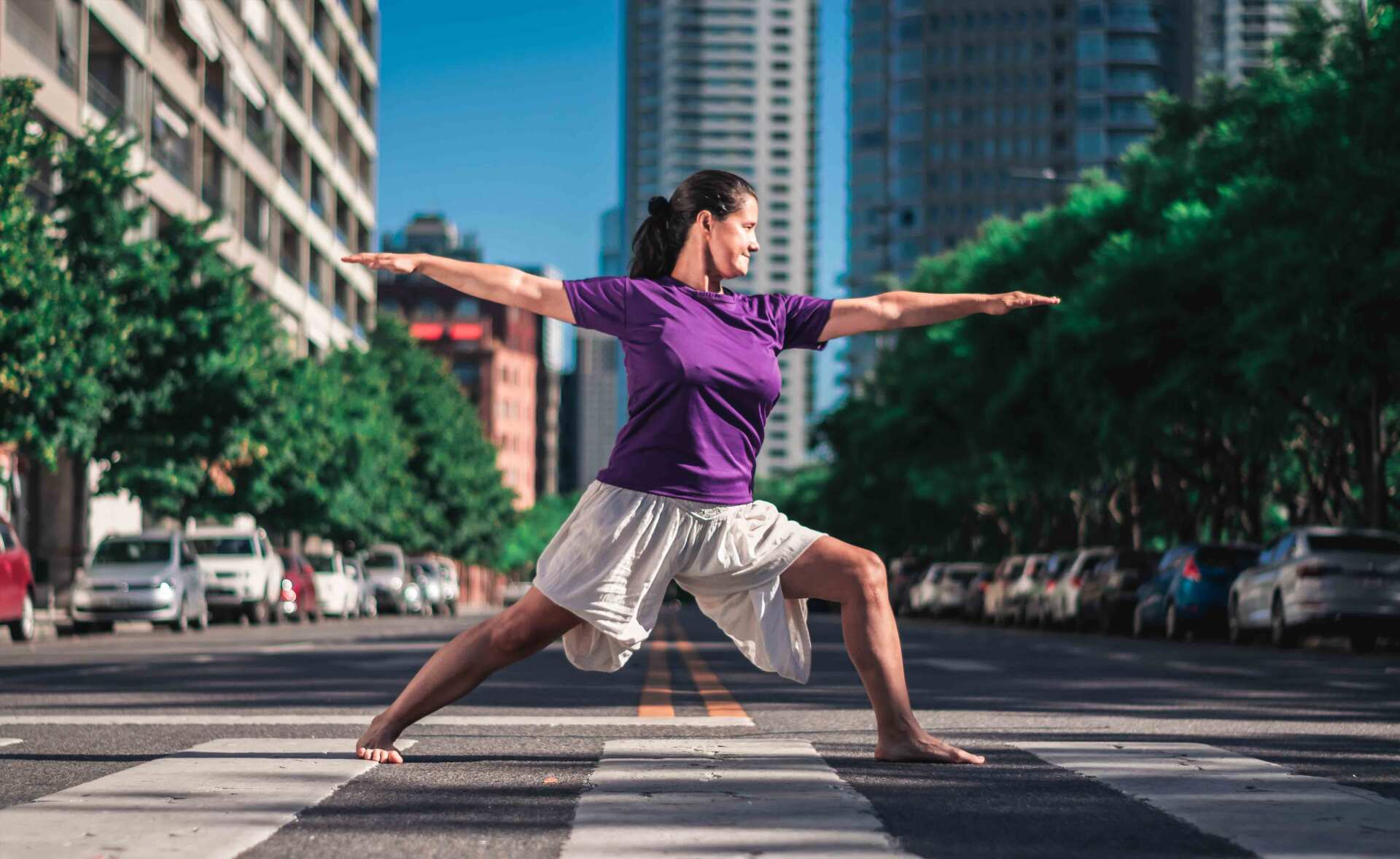 Mujer en pose de yoga en un cruce de peatones en una calle de la ciudad, con los brazos extendidos.