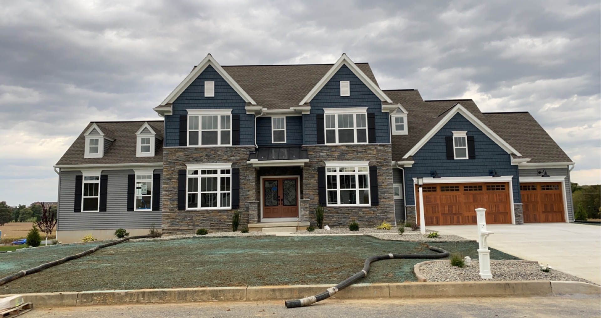Two-story blue and stone house with brown garage doors on a cloudy day.