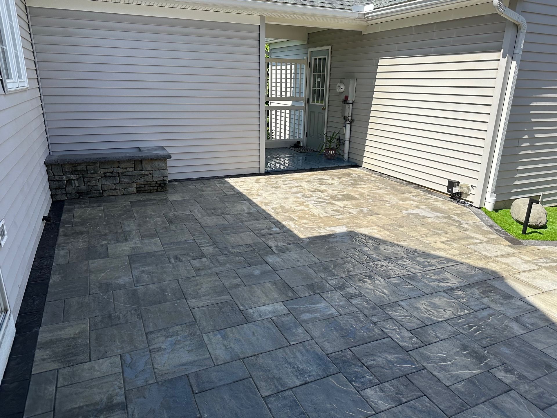 Patio with gray pavers, stone wall, and open door to a building with light siding.