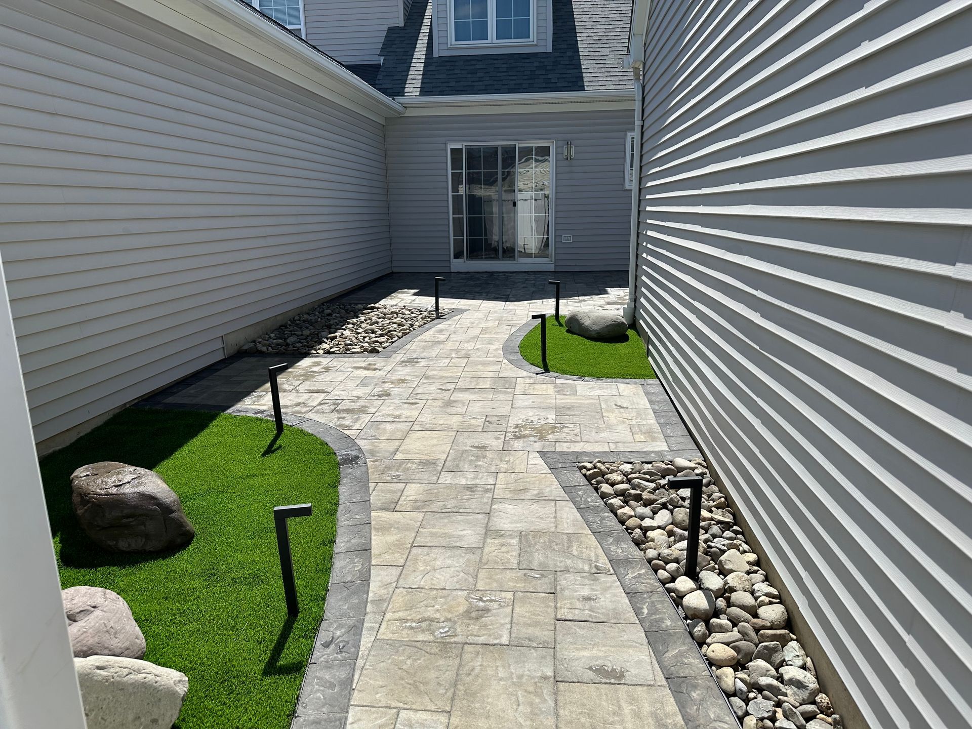 There is a paver walkway between two houses with grass and stone installed by complete property solutions of Lancaster PA