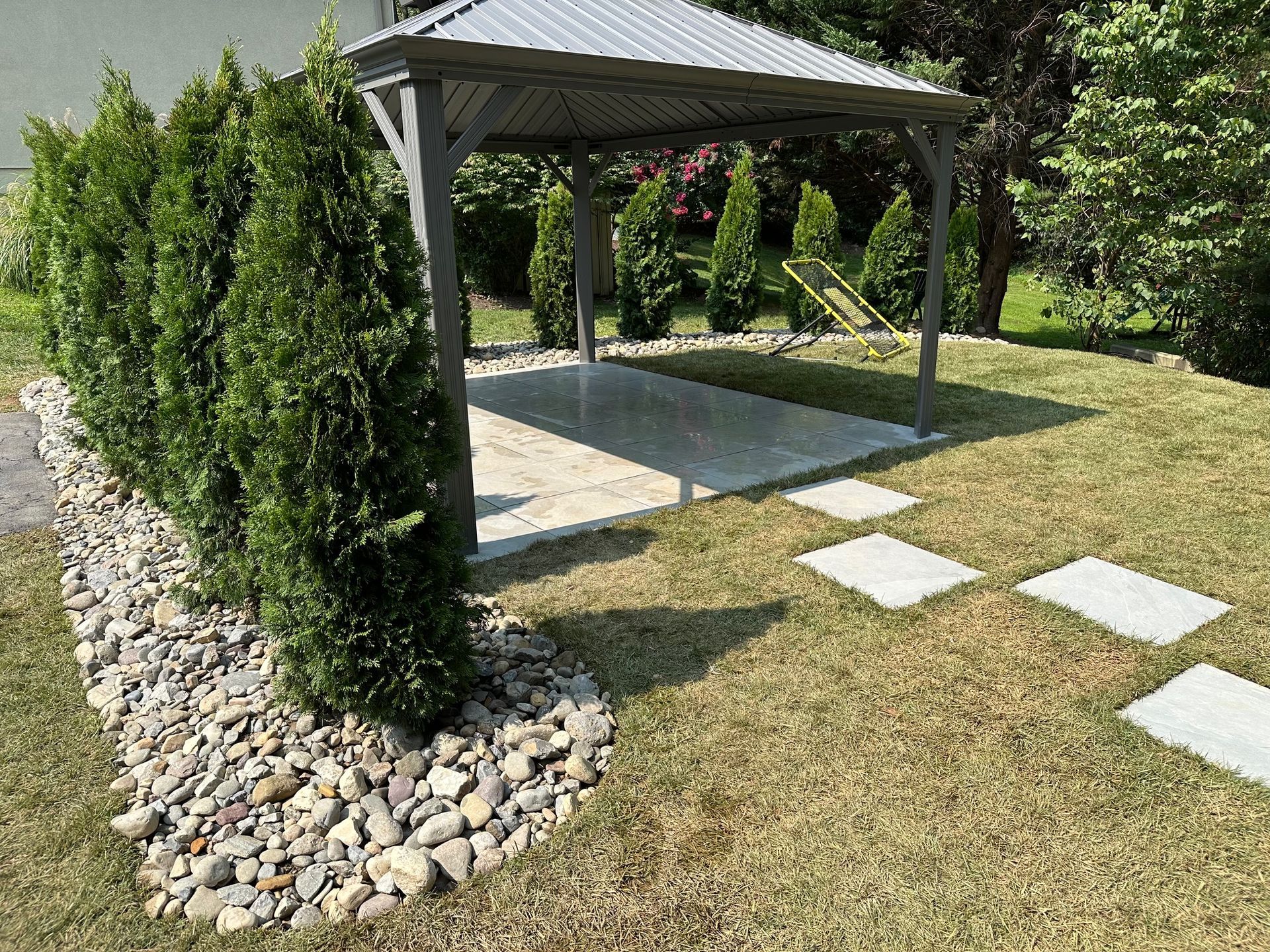 A gazebo is sitting on top of a lush green lawn next to a stone walkway by complete property solutions of Lancaster PA