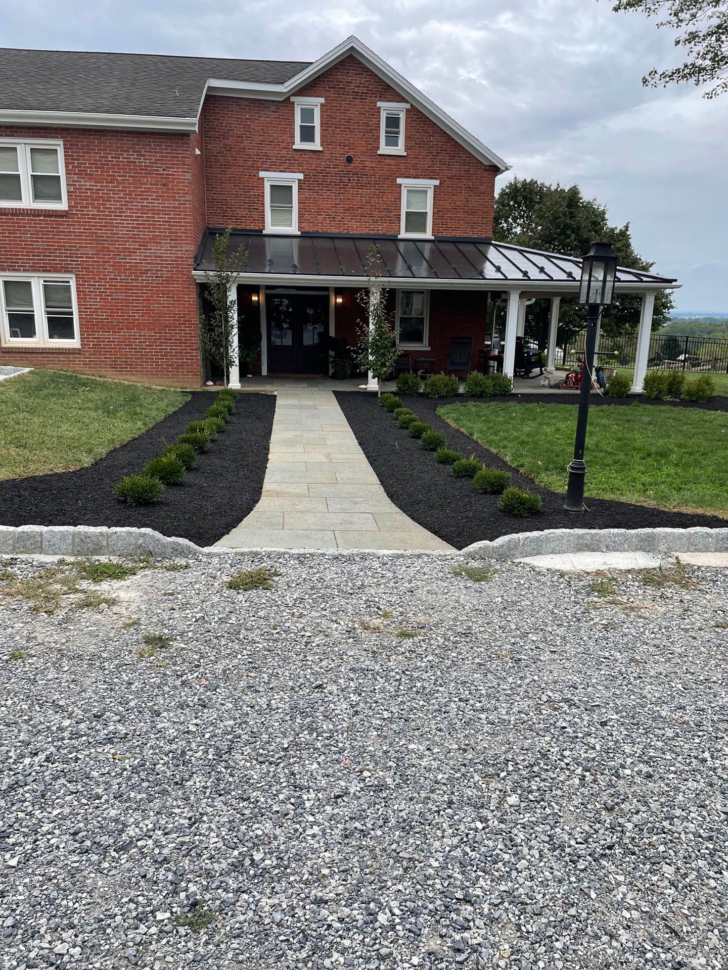 Red brick building with a stone path leading to the entrance, flanked by bushes and a gravel driveway.