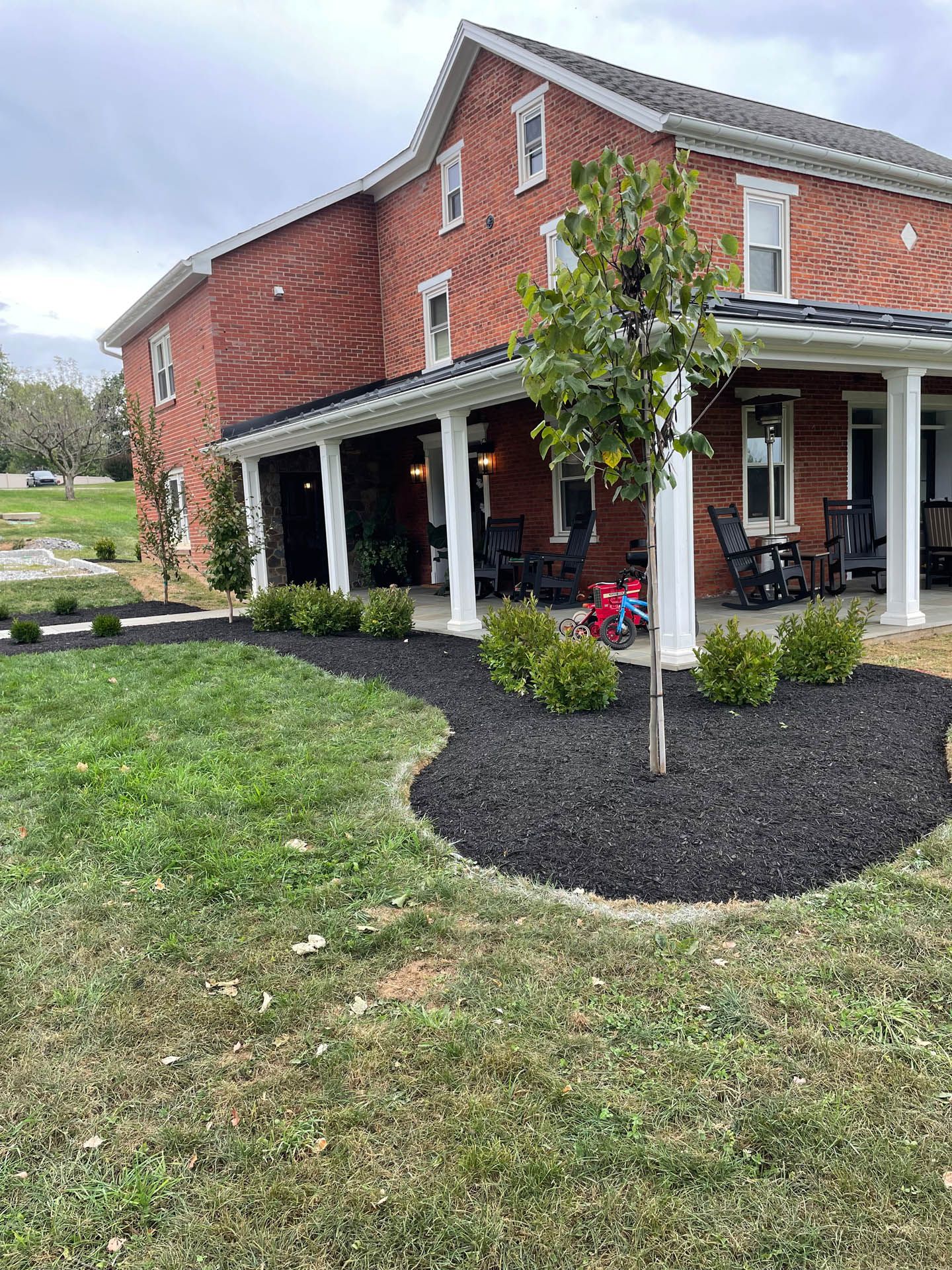 Red brick house with white porch, black mulch landscaping and small tree.