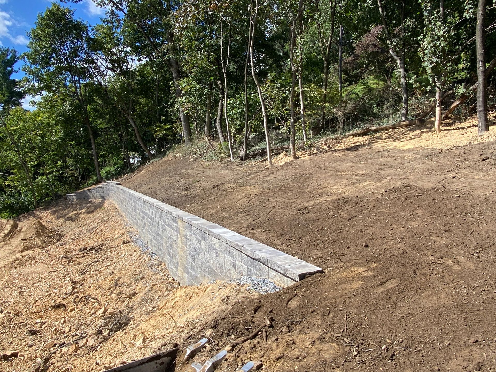 A concrete retaining wall is being built on top of a dirt hill installed by complete property solutions of Lancaster PA
