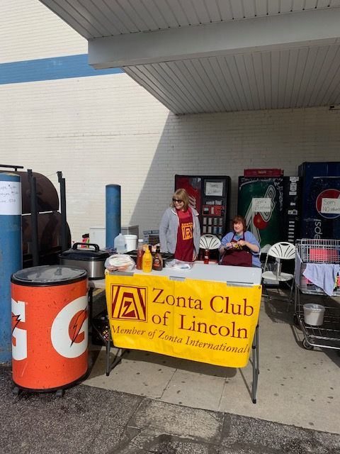 Zonta Club of Lincoln members at a fundraising food stand with hot dogs, condiments, and soda machines.