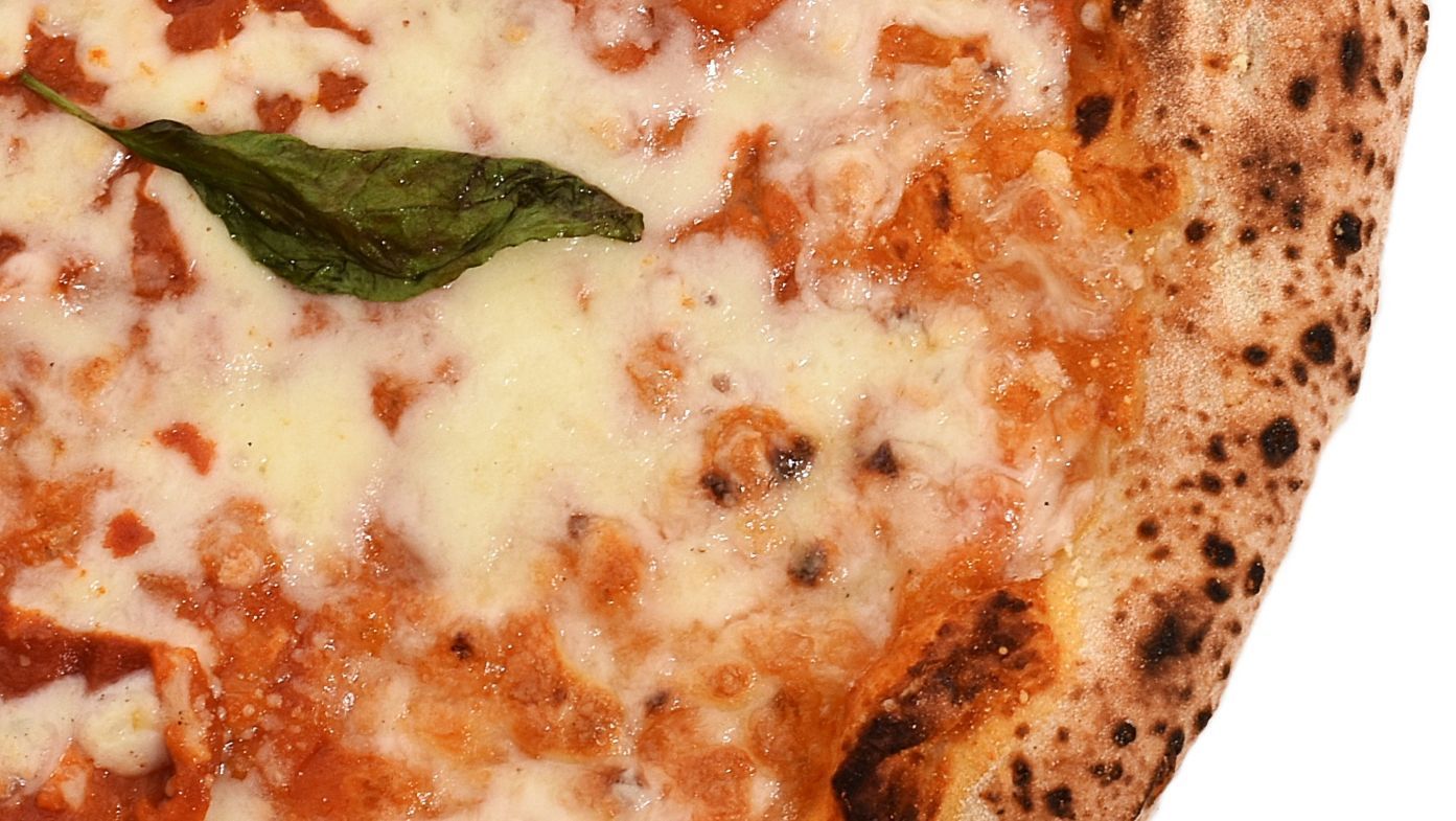 Close-up van een stuk kaaspizza met tomatensaus en een basilicumblaadje op de korst.