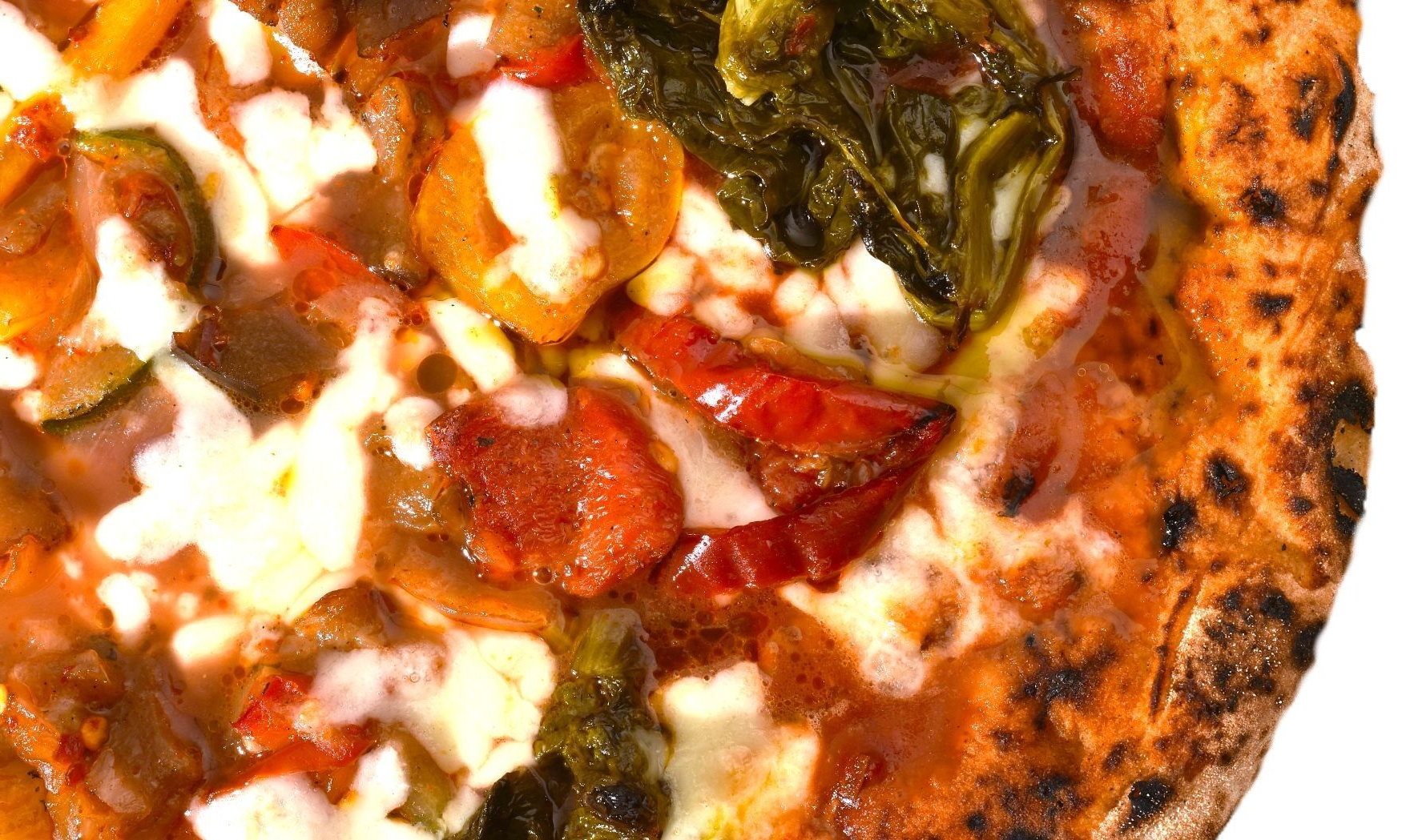 Close-up van een pizza met pepperoni, gesmolten kaas, groenten en een goudbruine korst.