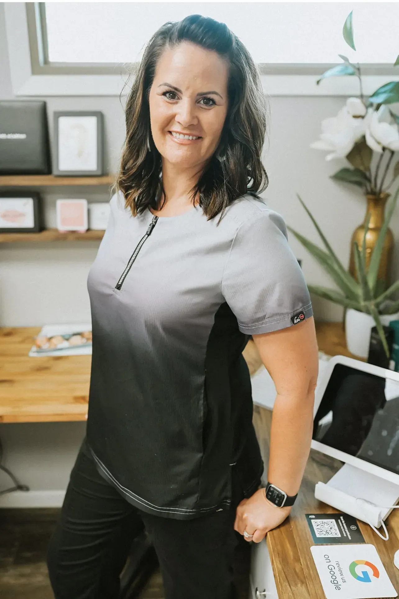 A woman in a scrub top is standing in front of a desk.