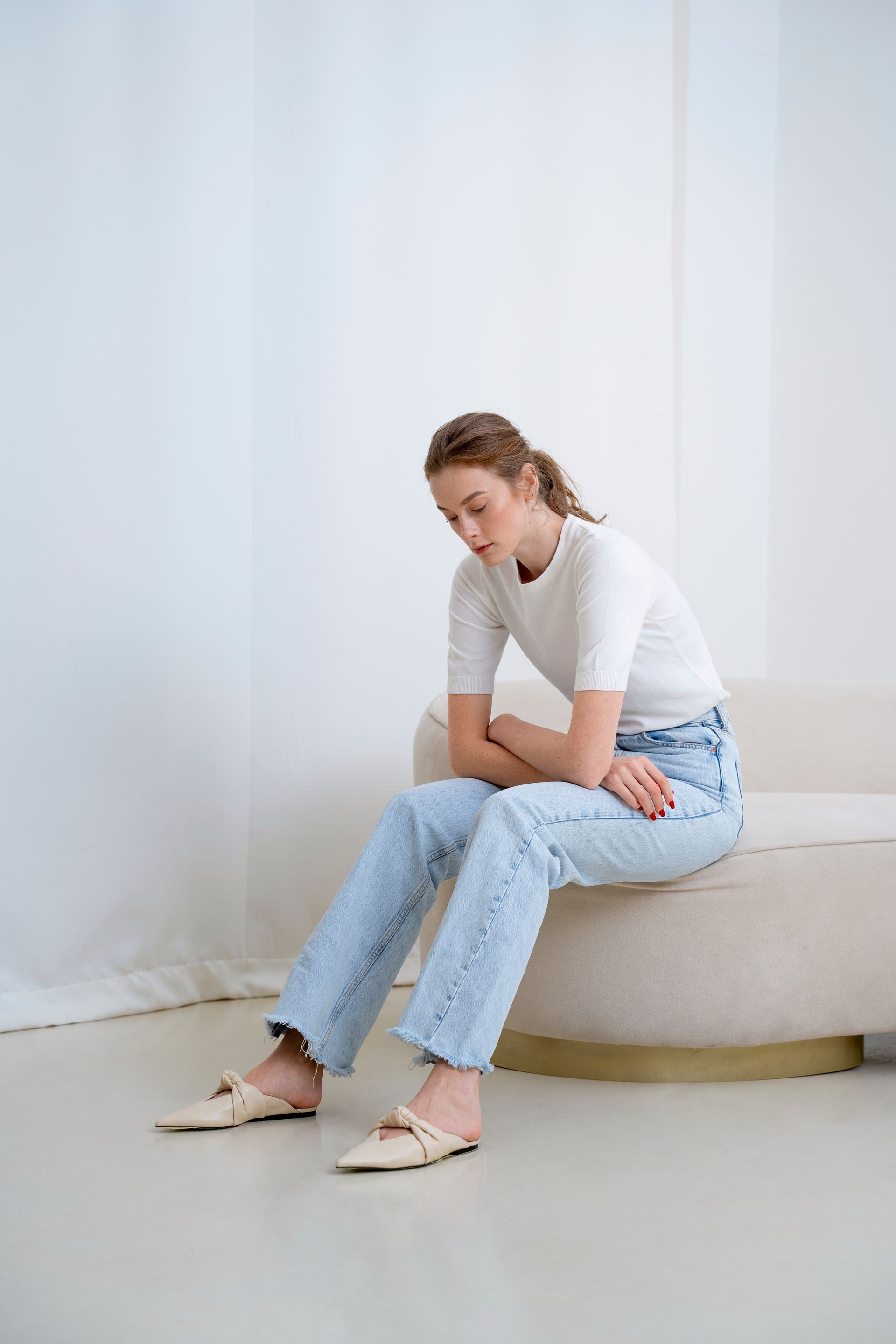 A woman is sitting on a couch wearing jeans and a white shirt.