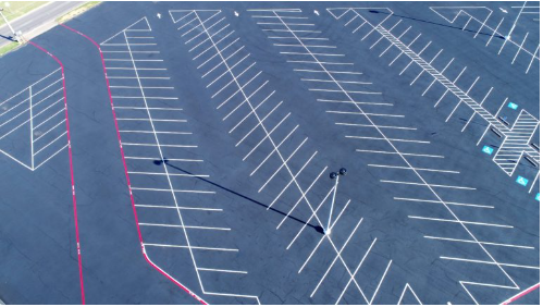 Aerial view of a large asphalt parking lot with white parking space lines and red painted borders.