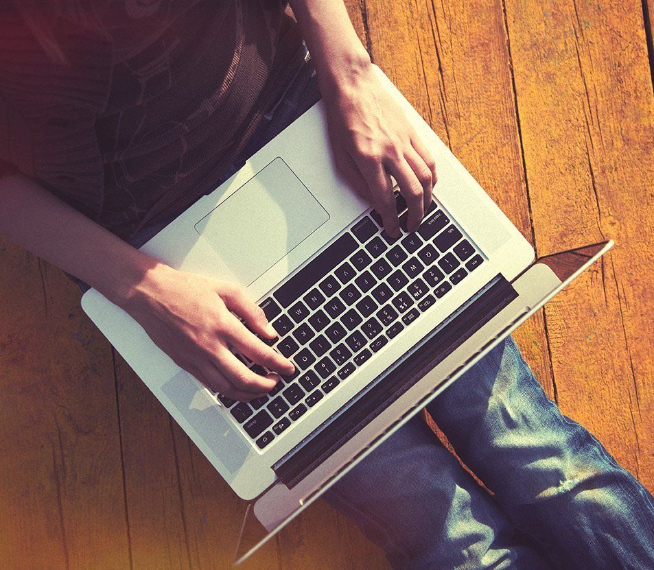 a person is typing on a laptop on a wooden floor.
