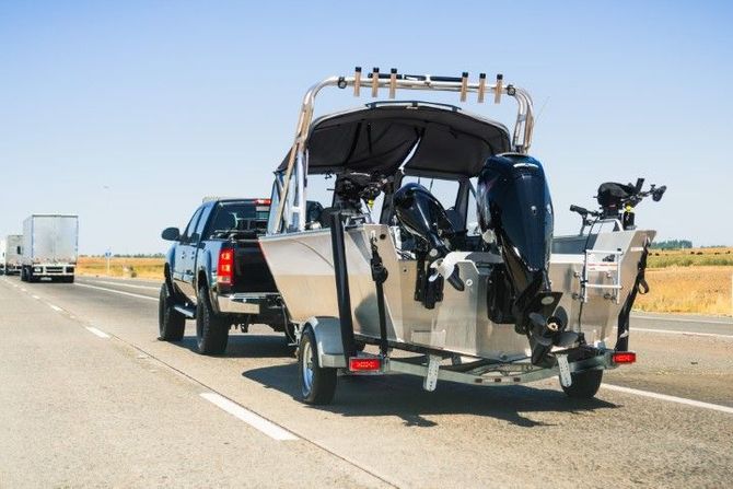 Black pickup towing a trailer carrying a damaged motorcycle on a highway under clear skies