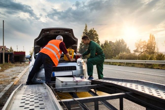 Workers loading equipment onto a flatbed truck on a roadside at sunset