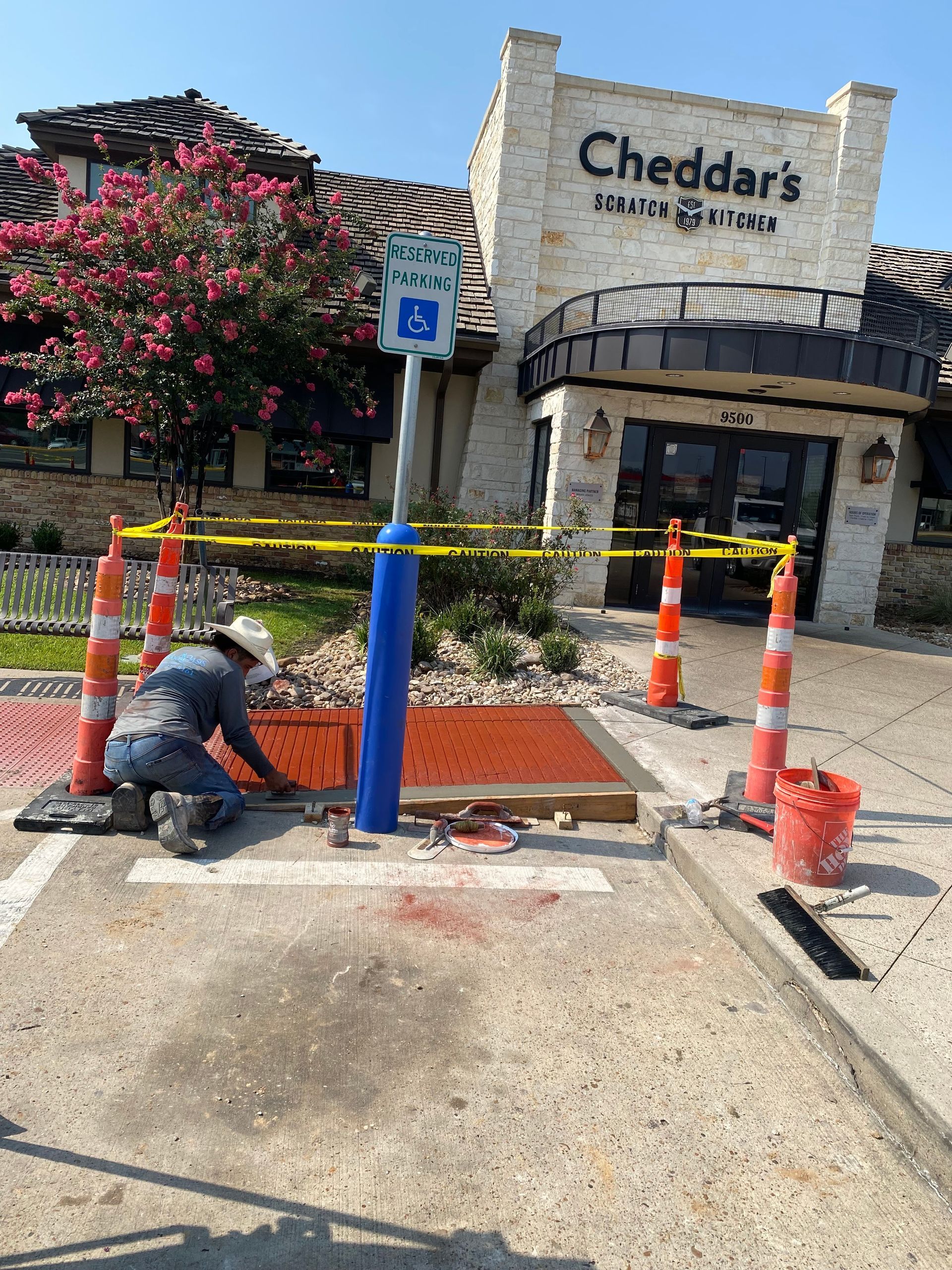 Person working at handicap parking spot in front of Cheddar's restaurant, marked by blue pole.