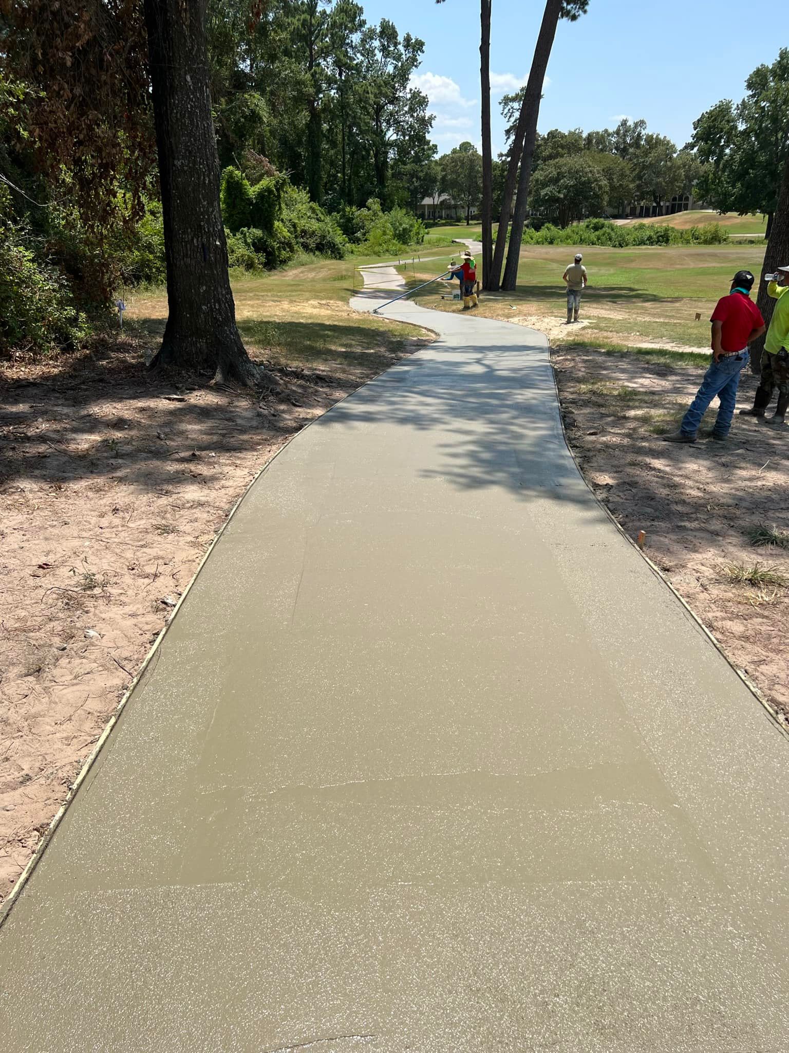 Workers near a freshly poured concrete path in a wooded park.