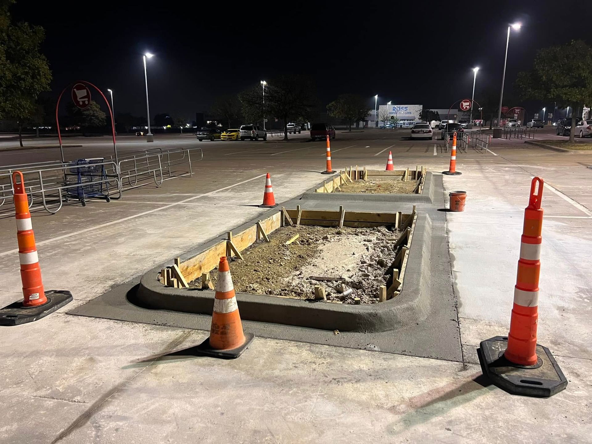 Construction in a parking lot at night. Two rectangular cement forms with orange traffic cones.