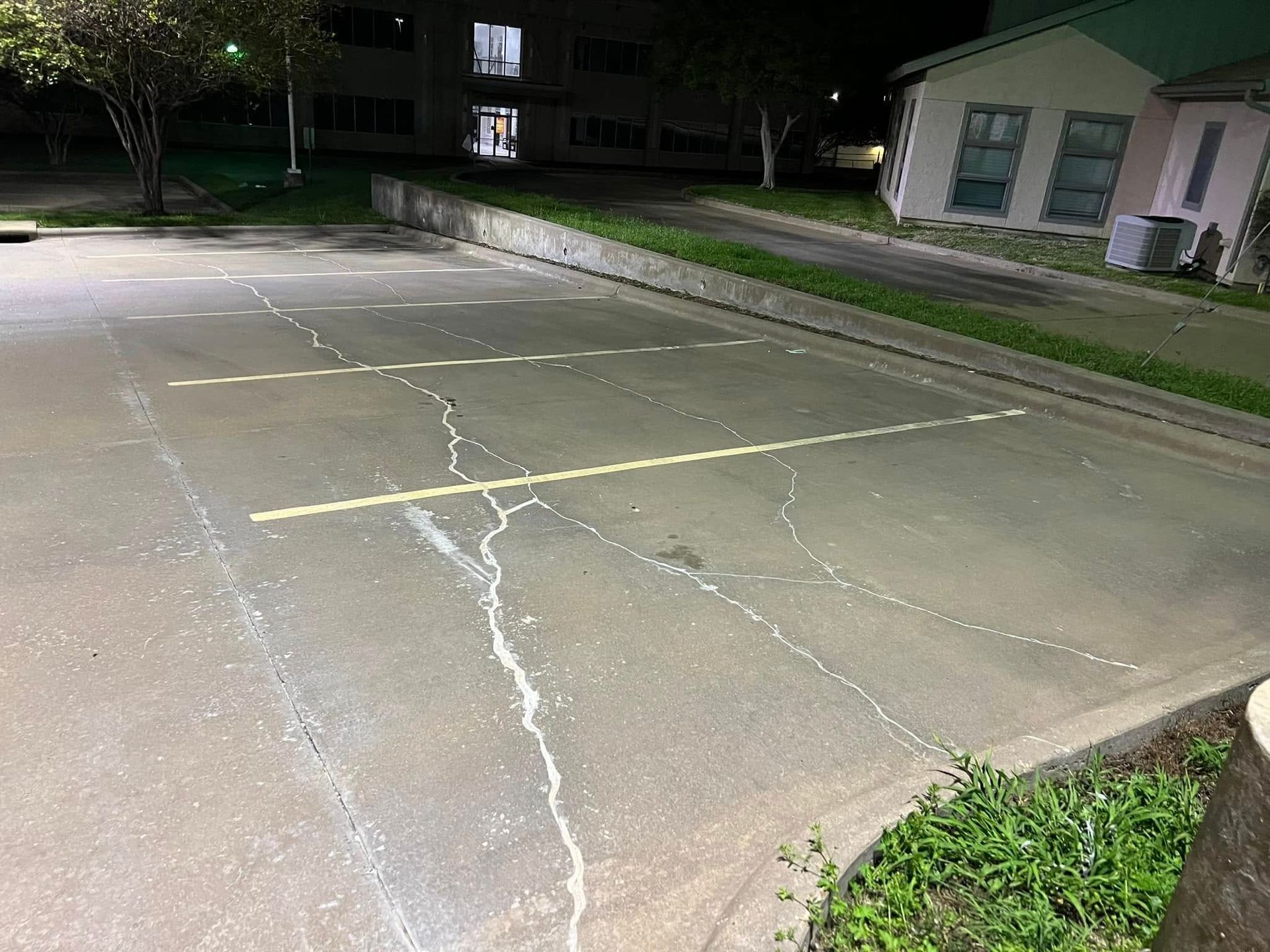 Cracked asphalt parking space with faded yellow lines, next to a concrete curb. Building in the background.