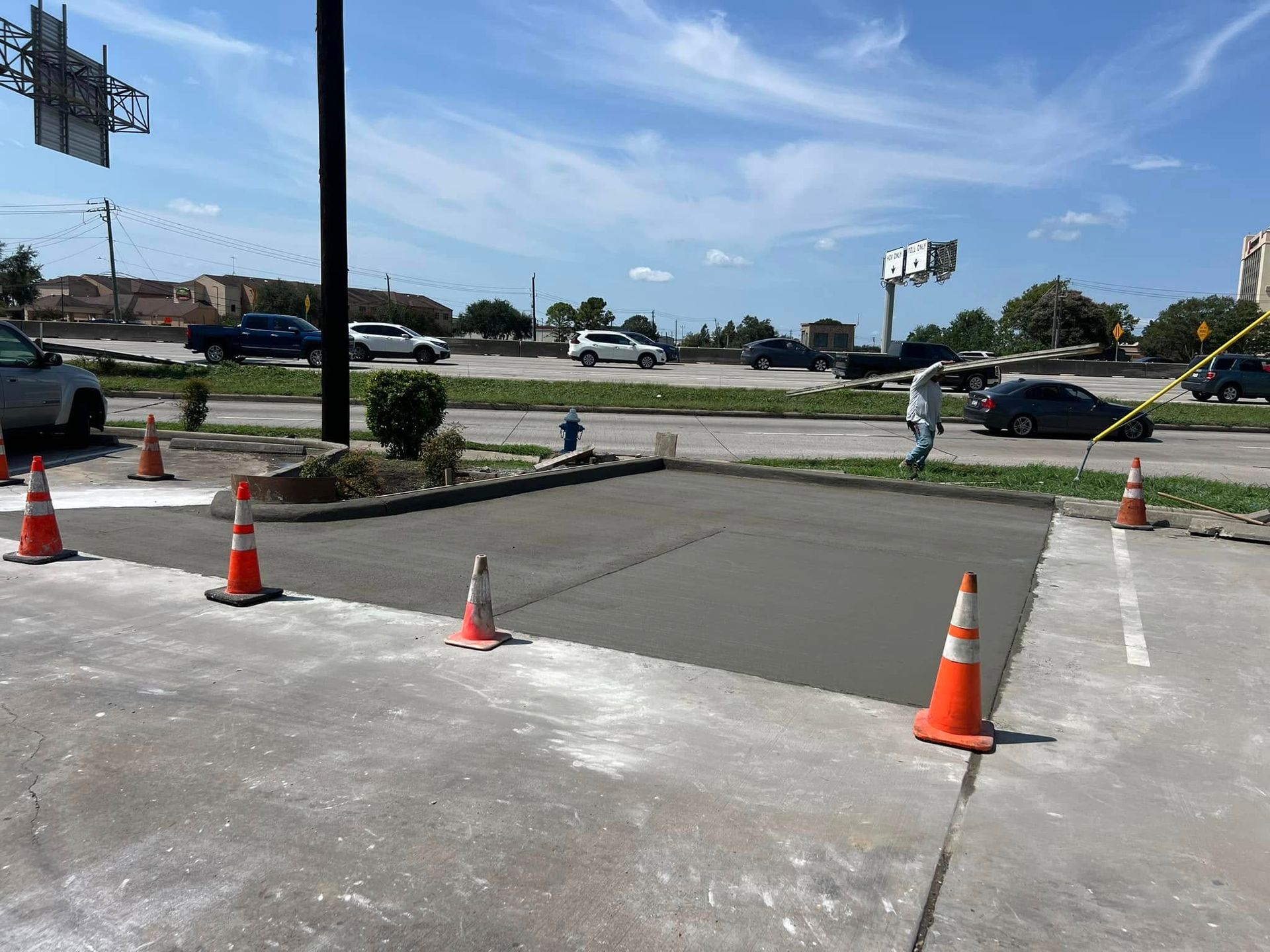 Freshly poured concrete area, bordered by orange cones, at a commercial property's driveway. 