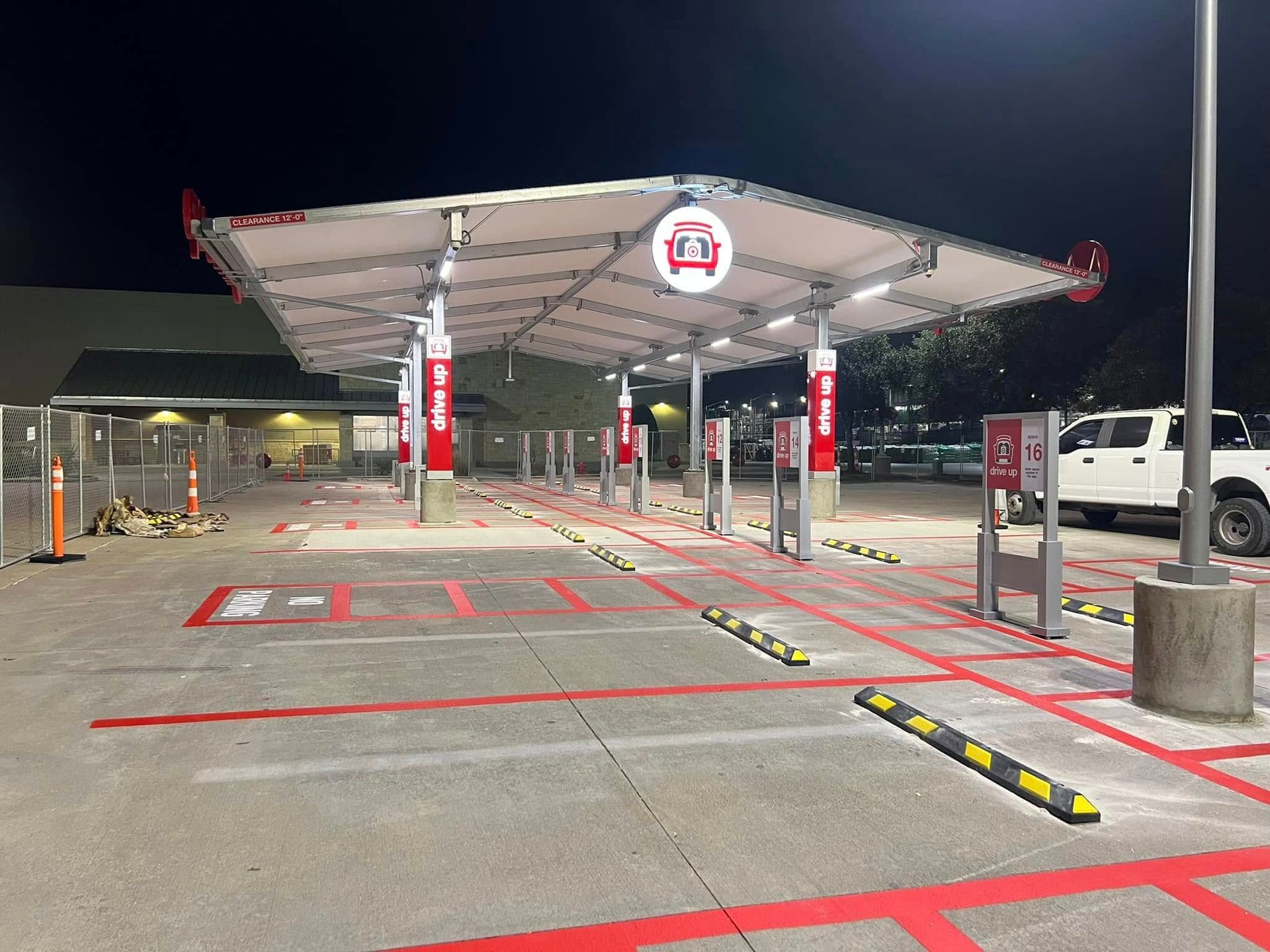 Drive-thru at night: Canopy over ordering stations with red accents, concrete, and a white pickup truck.