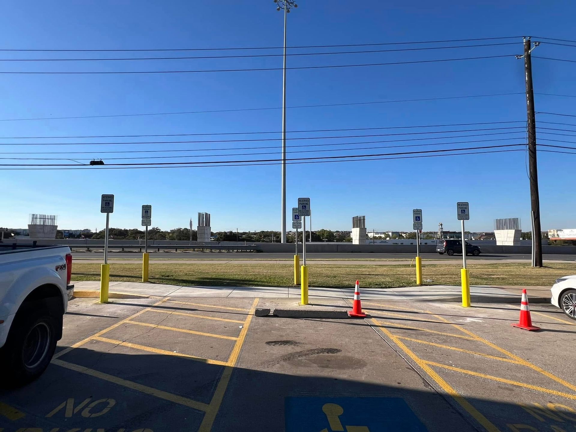 Parking spaces with signage, including accessible parking. Cars and a truck parked in the spots. Blue sky overhead.