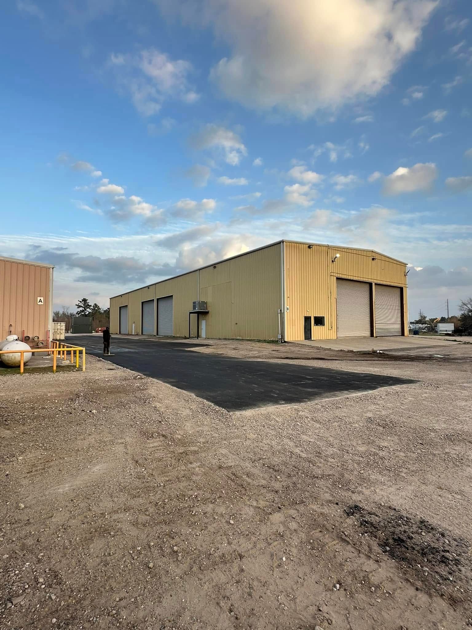 Yellow industrial building with several closed garage doors under a cloudy blue sky.