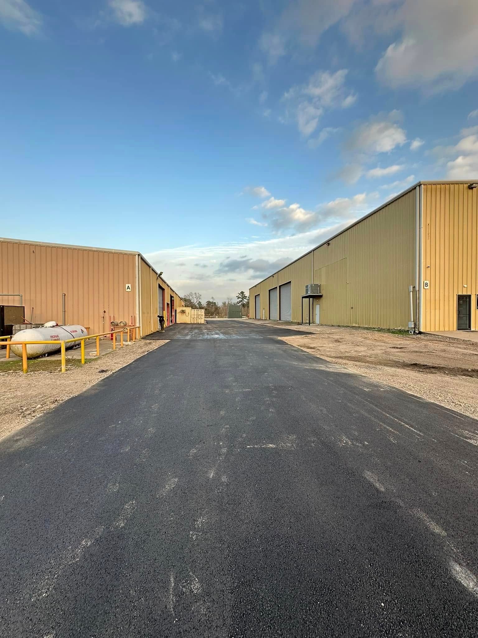 Paved road between two industrial buildings under a cloudy sky.