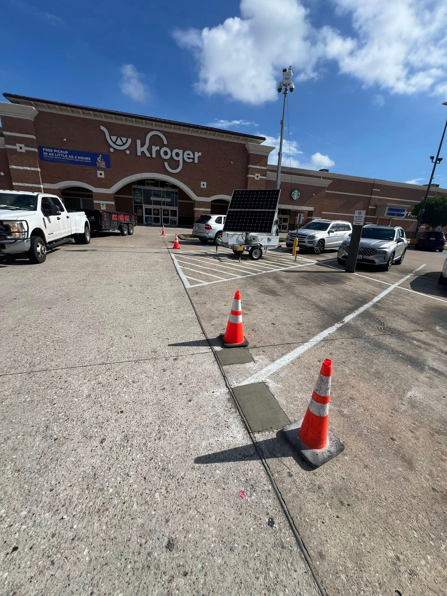 Kroger grocery store exterior, with a white truck, parked cars, and orange traffic cones. A solar panel is present.