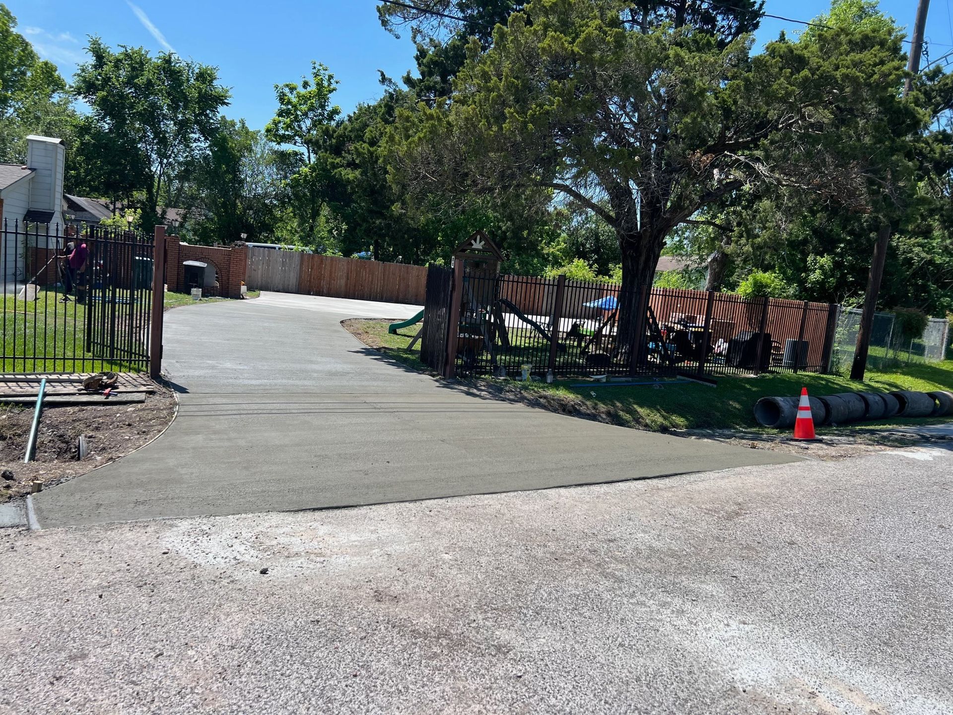 Newly poured concrete driveway leading to a house, with a gravel road in the foreground.