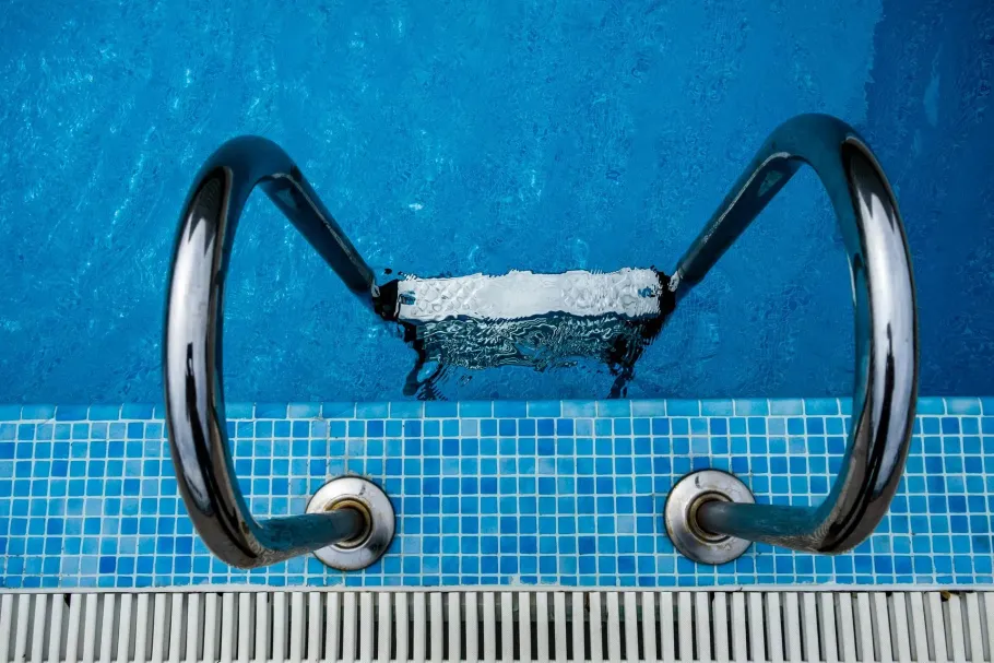Stainless steel ladder steps in a blue tiled swimming pool.