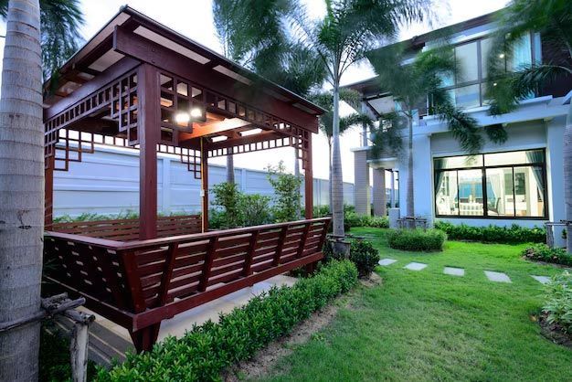 Modern resort courtyard with a wooden gazebo, palm trees, and green lawn beside a building.