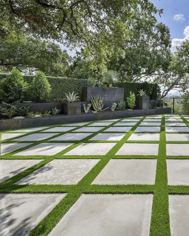 Modern garden patio with large square stone pavers and grass joints under leafy trees