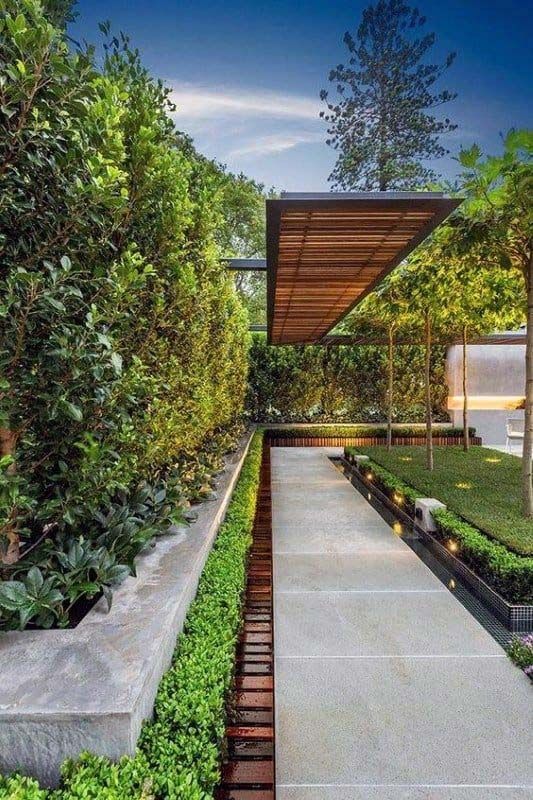 Modern garden walkway with concrete path, lush greenery, and a wooden pergola overhead