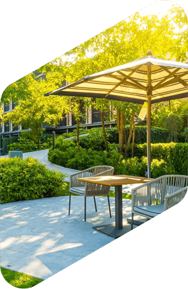 Outdoor patio with table, chairs, and beige umbrella in a green garden courtyard under bright sunlight
