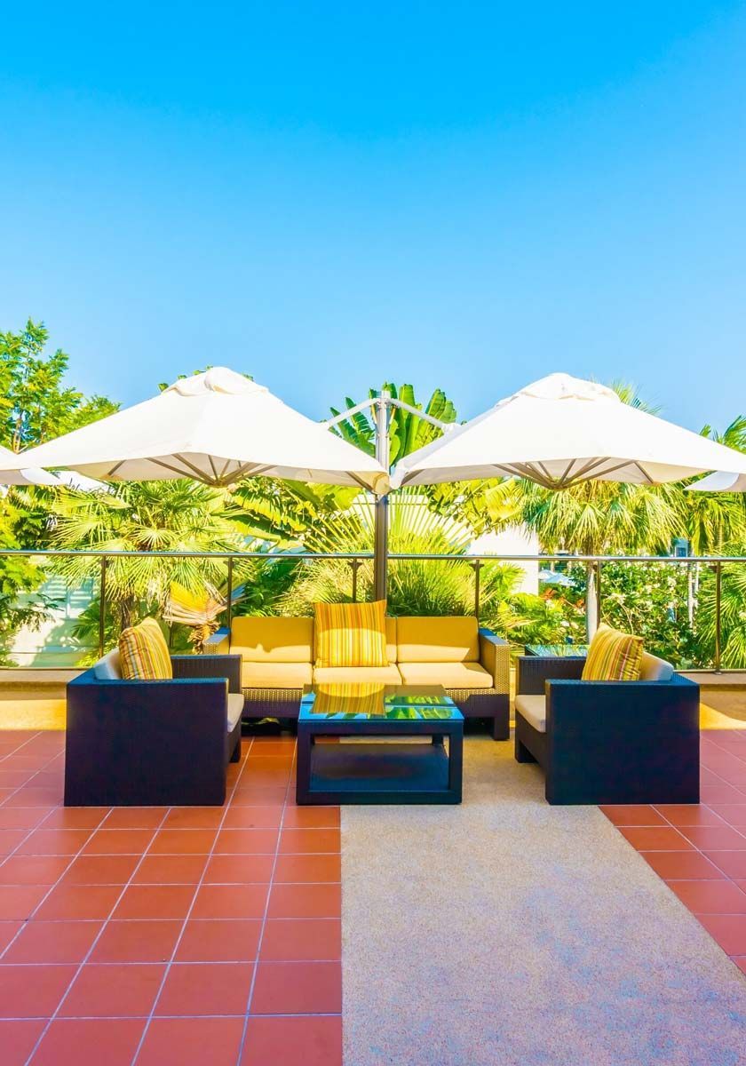 Patio lounge with white umbrellas, dark sofas, and yellow cushions on a terracotta terrace overlooking greenery