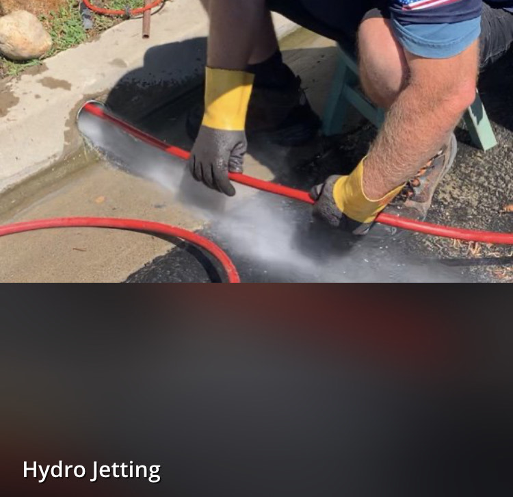 A man wearing yellow gloves is using a red hose for hydro jetting