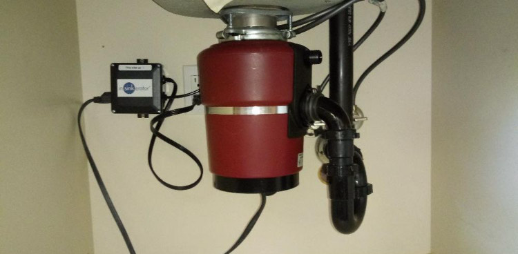 A red garbage disposal is attached to a sink.