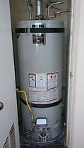 A water heater is sitting in a closet next to a door.