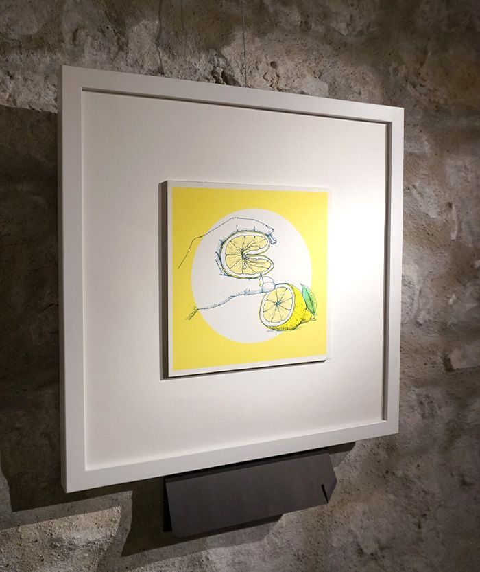 Zitronenfalter Eine Illustration im weißen quadratischen Bilderrahmen, es zeigt eine Zitrone das von einer Hand gefaltet wird. Ein zitronengelber Hintergrund unterstreicht das Bild.