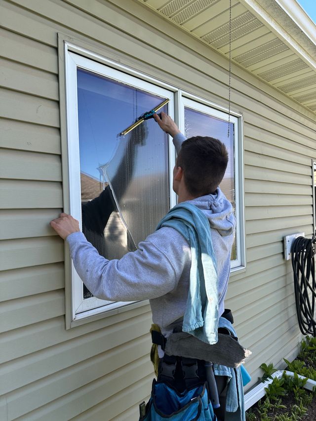 Worker cleaning a window with a hose outside a beige house