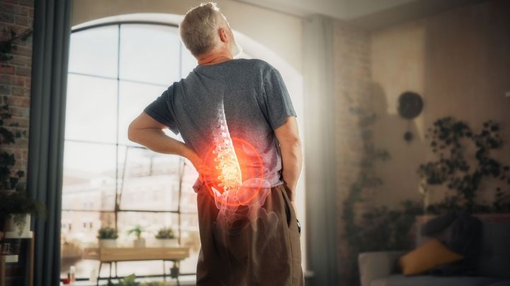 A man is standing in a living room holding his back in pain A man is standing in a living room holding his back in pain