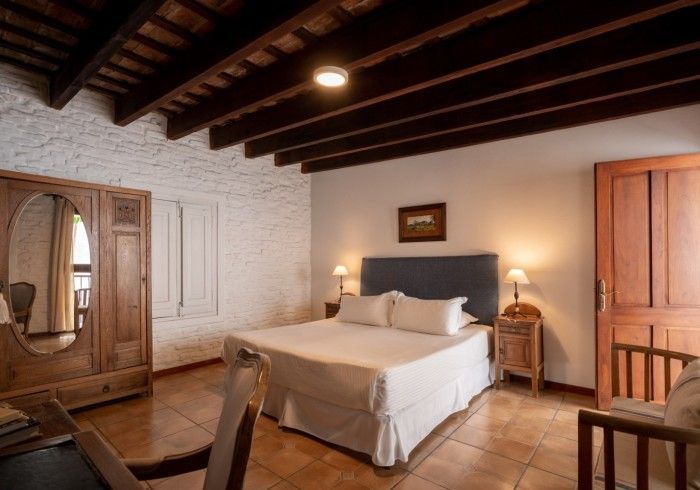 Dormitorio con cama, muebles de madera, pared de ladrillo y vigas a la vista.