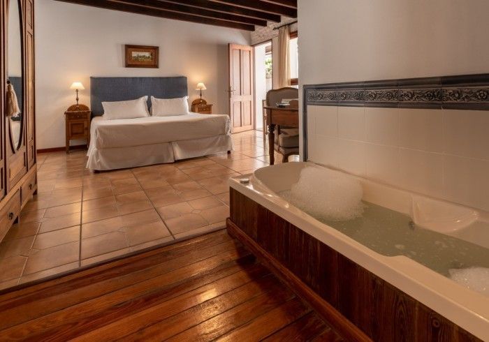 Dormitorio con cama, bañera llena de burbujas y suelo de madera.