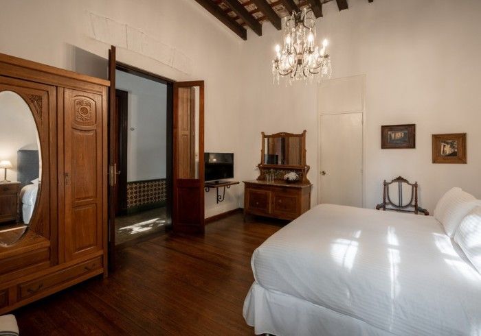 Dormitorio con cama grande, muebles de madera, lámpara de araña y puerta abierta a un baño.