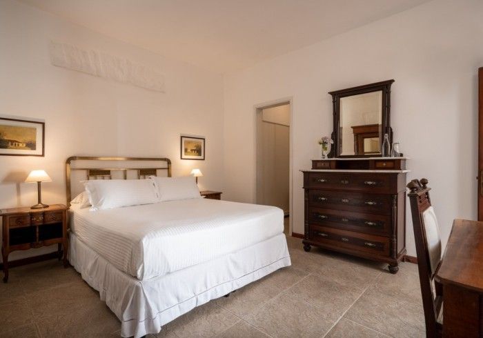 Dormitorio con cama, cómoda, mesita de noche y escritorio. Paredes blancas y muebles de madera.