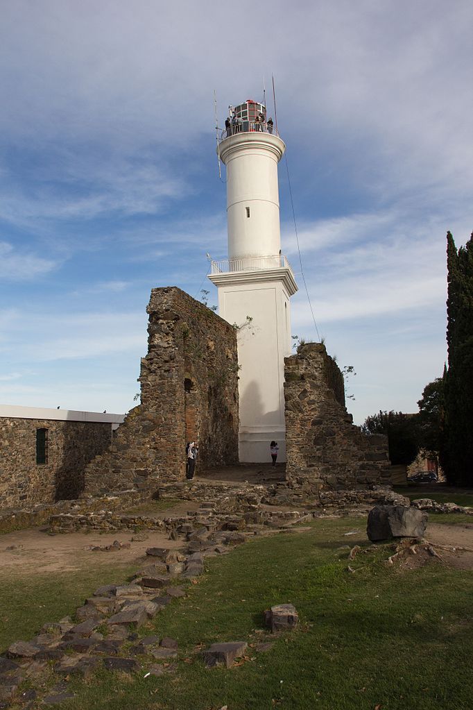 Un faro blanco se alza entre ruinas contra un cielo azul.