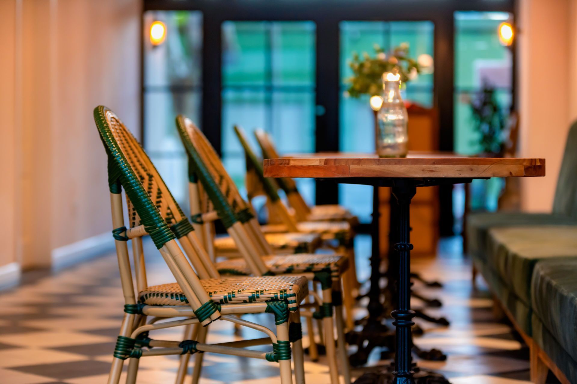 Fila de sillas de mimbre verdes y beige y una mesa dispuesta para cenar, en el interior.