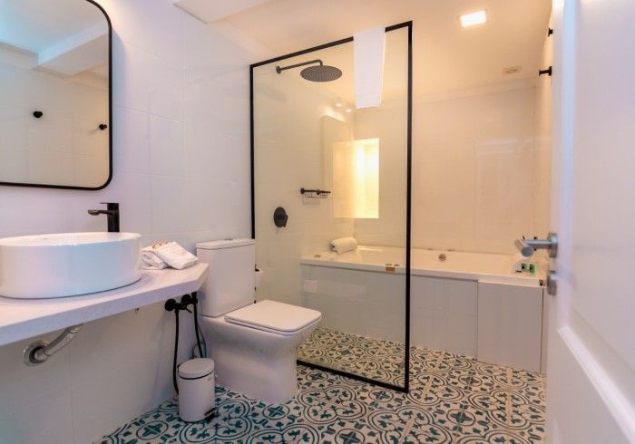Baño moderno con paredes blancas, detalles en negro, ducha de cristal y suelo de baldosas estampadas.
