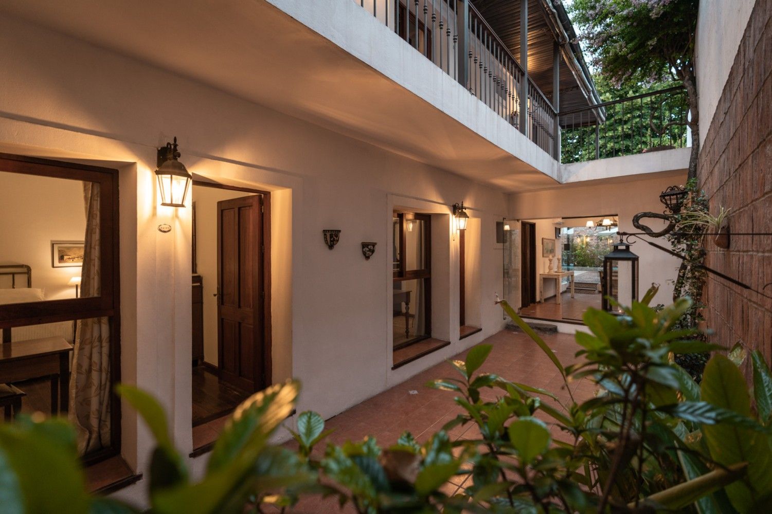 Patio con un edificio de dos plantas, con puertas abiertas, ventanas y lámparas colgantes.