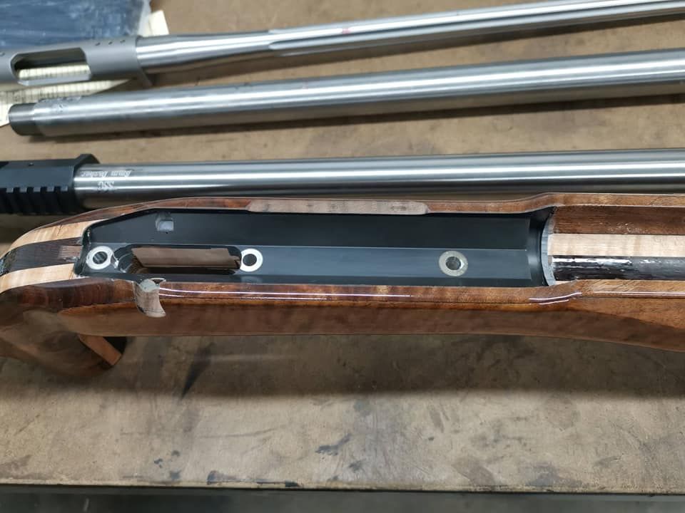 Close-up of a rifle stock with black mounting hardware and metal rods on a workbench