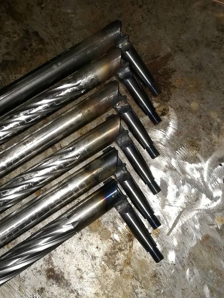 Metal drill bits arranged diagonally on a dirty surface, with silver shafts and dark shanks.
